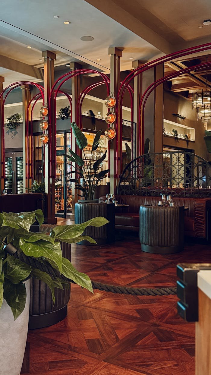 Stylish restaurant interior with wooden flooring, red arches, and lush plants.